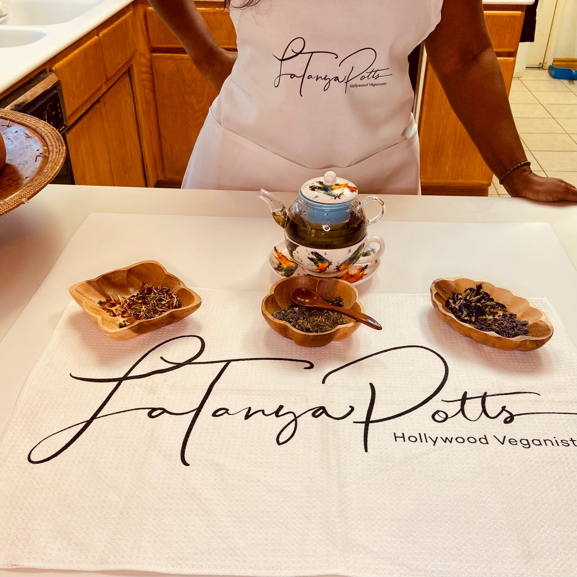 LaTanya Potts in a branded apron preparing loose-leaf tea in a glass teapot
